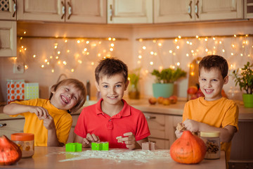 waiting for the holiday! Three happy brothers make gingerbread cookies in the kitchen, have fun and laugh. next to them on the table are pumpkins