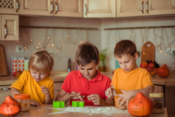 Fototapeta premium waiting for the holiday! Three happy brothers make gingerbread cookies in the kitchen, have fun and laugh. next to them on the table are pumpkins