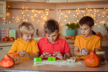 Fototapeta premium waiting for the holiday! Three happy brothers make gingerbread cookies in the kitchen, have fun and laugh. next to them on the table are pumpkins