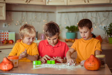 Fototapeta premium waiting for the holiday! Three happy brothers make gingerbread cookies in the kitchen, have fun and laugh. next to them on the table are pumpkins