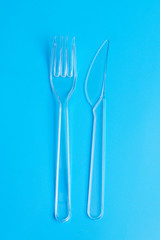 Plastic disposable tableware, cutlery. Fast food. Clean plastic fork and knive on blue background. Disposable dishes, environmental pollution. Top view, flat lay.