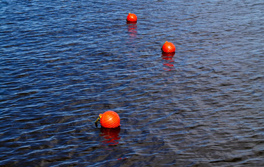 Three bright orange buoys floating on lake water surface. Set of three orange safety buoys in a lake with small waves on water surface.