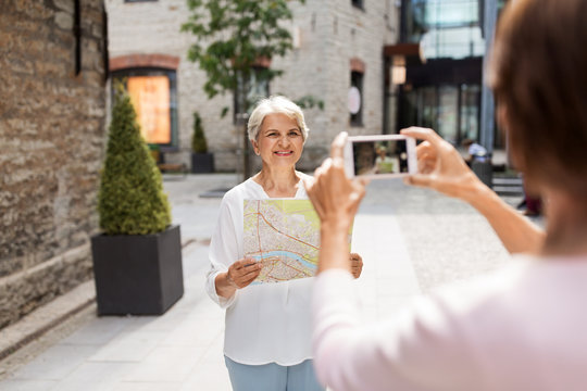 tourism, travel and friendship concept - happy senior woman with city map being photographed by her friend on street in tallinn