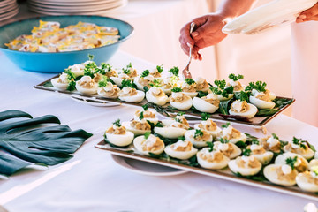 close up of hand taking some eggs with vegetables and sauce - catering full of food in a party - restaurant and wedding event  people taking food from dishes