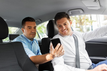 transportation, vehicle and technology concept - middle aged male passenger on back seat showing his smartphone to car driver