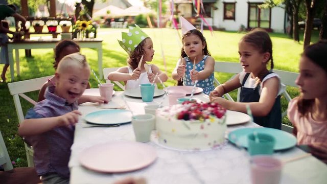 Down syndrome child with friends on birthday party outdoors in garden.