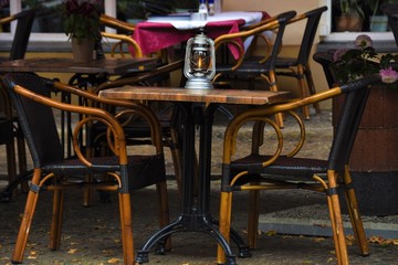 wooden table and chairs for eating near an outdoor restaurant, a candle in a glass candlestick and a flower in a pot
