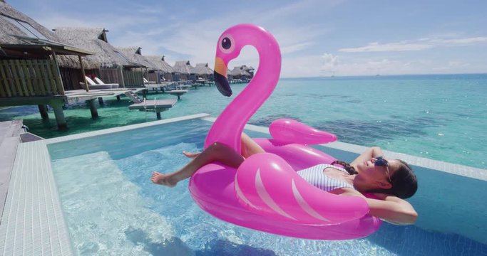 Beach Pool Holidays Vacation Woman in bikini in inflatable pink flamingo toy mattress float in pool. Girl relaxing sunbathing enjoying travel holidays at resort pool living Luxury lifestyle travel.