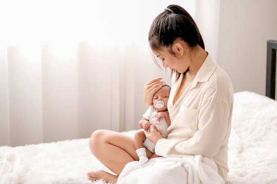 Soft blur image of beautiful Asian mother hold her newborn baby with baby teat on the white bed.