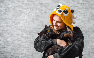 portrait of young teenager brunette girl with long hair holding in her arms black cat on gray wall background