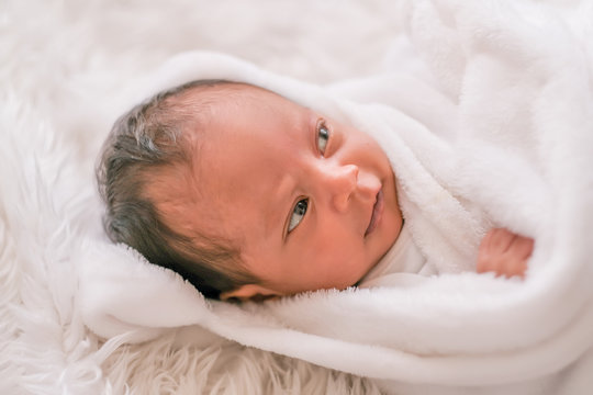 Soft blurred image of Asian newborn baby cover by white cloth on white bed and smile to show emotion of relax and happy.