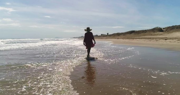 dron sigue a muchacha que se recoge el vestido para no mojarse andando en orilla de playa dorada
