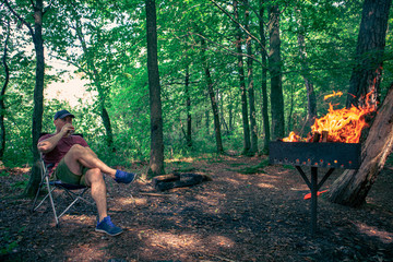man sitting in camp chair drinking beer bbq fire