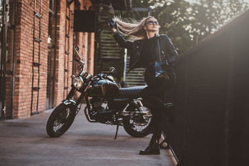 Fototapeta na wymiar Blond female biker is posing for photographer next to black, shiny chopper.