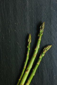 Three asparagus spears lay on a black slate countertop