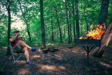 man sitting in camp chair drinking beer bbq fire