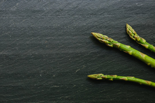 Close up of three asparagus tips on black slate countertop