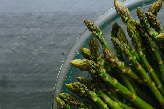 Close up of asparagus tips in bowl on slate countertop