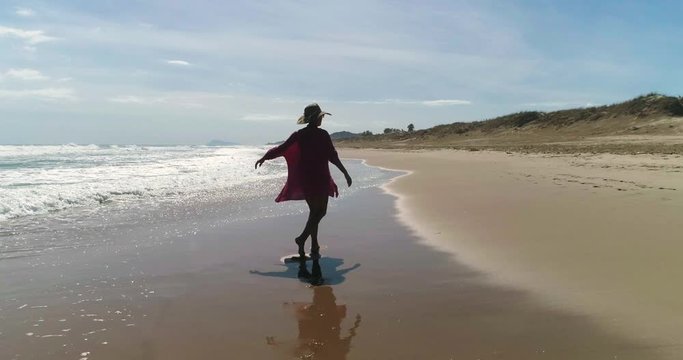 Muchacha feliz dando vueltas en la orilla de playa junto a dron