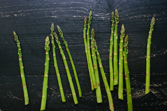 Fresh cut asparagus spears lay on a black painted rustic wooden table