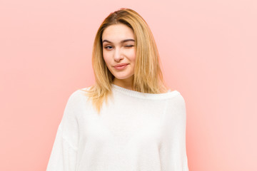 young pretty blonde woman looking happy and friendly, smiling and winking an eye at you with a...