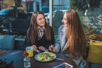 two girlfriends talking while eating in outdoors cafe autumn time