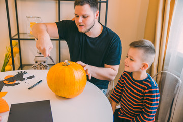 young father with toddler son making jack pumpkin head for halloween holiday