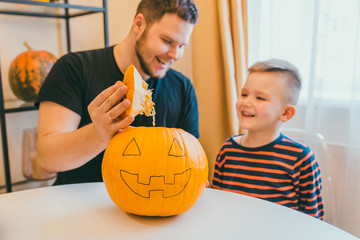 young father with toddler son making jack pumpkin head for halloween holiday