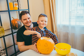 young father with toddler son making jack pumpkin head for halloween holiday