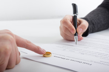 Hands of wife, husband signing decree of divorce, dissolution, canceling marriage, legal separation documents, filing divorce papers or premarital agreement prepared by lawyer. Wedding ring