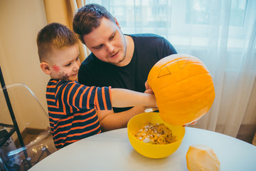 young father with toddler son making jack pumpkin head for halloween holiday