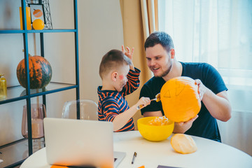 young father with toddler son making jack pumpkin head for halloween holiday