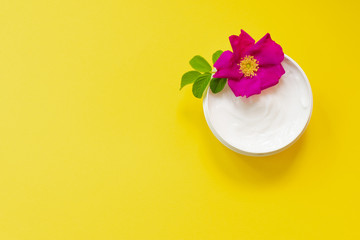 White soft cream in a jar on bright yellow background with dog rose, top view, anti-ageing moisturizing cream with dog rose oil essential and vitamin E