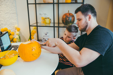 young father with toddler son making jack pumpkin head for halloween holiday