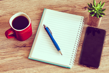 Blank notebook with cell phone and cup of coffee on wooden background.