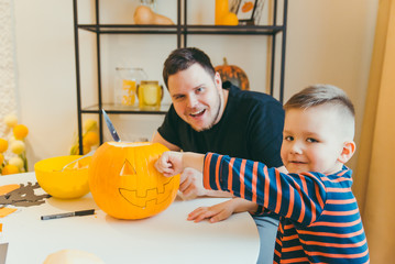 young father with toddler son making jack pumpkin head for halloween holiday