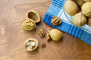 Whole walnuts and walnut kernel halves without shell on a dark wooden table and checkered towel,...