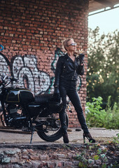 Obraz na płótnie Canvas Portrait of mature attractive lady next to her vintage motorbike and graffiti brick wall.