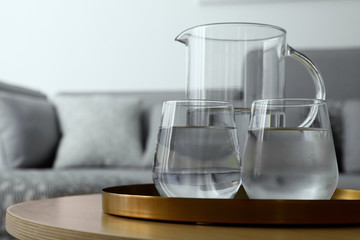 Tray with jug and glasses of water on table in room, space for text. Refreshing drink