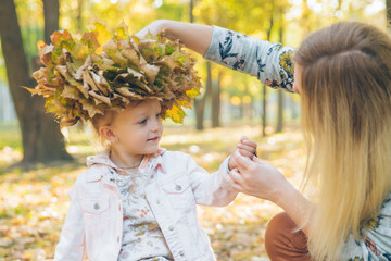 young mother make maple leaf wreath for little toddler daughter