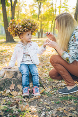 young mother make maple leaf wreath for little toddler daughter