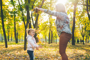 mather with little toddle daughter playing in autumn city public park