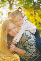 piggyback mother playing with daughter at autumn city park