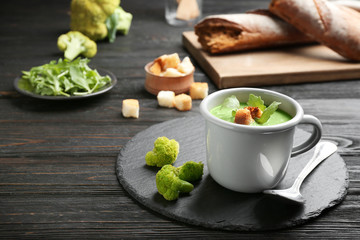 Cup of broccoli cream soup with croutons served on black wooden table, space for text