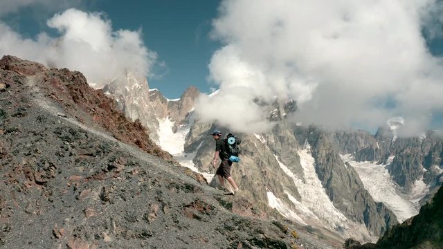 A man goes uphill, against the backdrop of Ushba