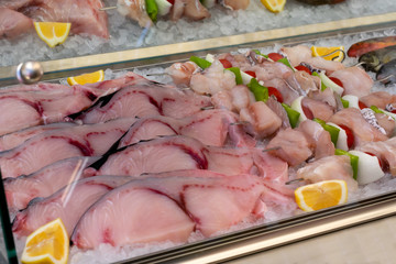 Raw fresh sliced fish filet kebabs with fish and vegetables with lemon pieces on the ice in the refregerator. Seafood on the ice in greek market.