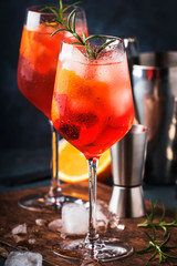 Milano spritzer alcoholic cocktail with red bitter, dry white wine, soda, zest and ice. Dark blue background, bar tools, selective focus