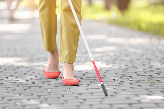 Blind woman with cane walking on city street, closeup