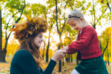 young mother make maple leaf wreath for little toddler daughter