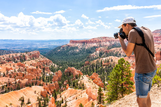 Man tourist person taking picture of view with camera at Sunset Point Overlook cliff rim edge at Bryce Canyon National Park in Utah